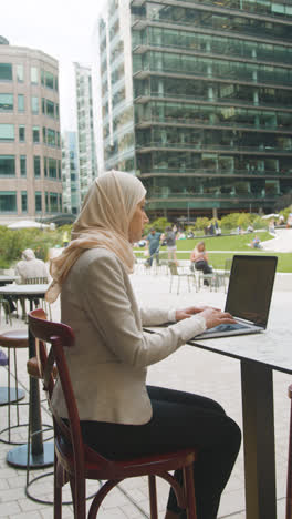 Vertikales-Video-Einer-Muslimischen-Geschäftsfrau,-Die-Draußen-In-Stadtgärten-Sitzt-Und-Am-Laptop-Arbeitet